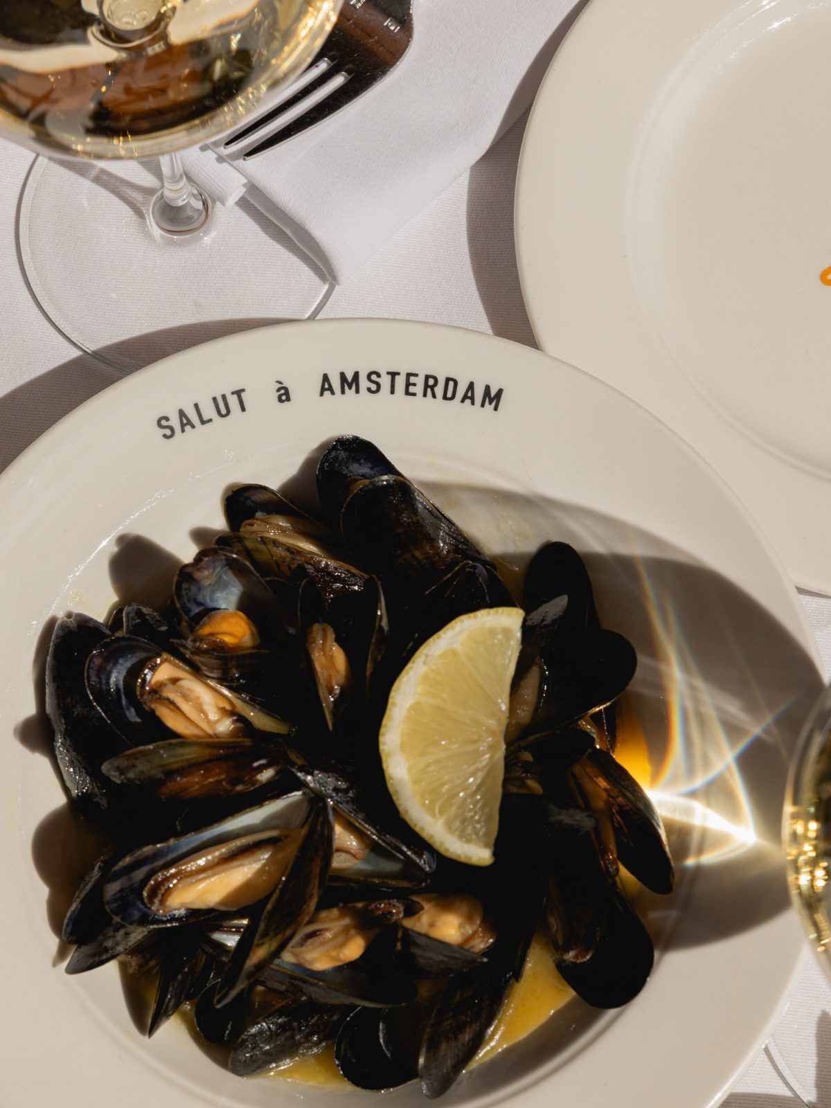 Moules Pastis with beurre blanc and lemon in a Salut bowl, with a glass of white wine beside it
