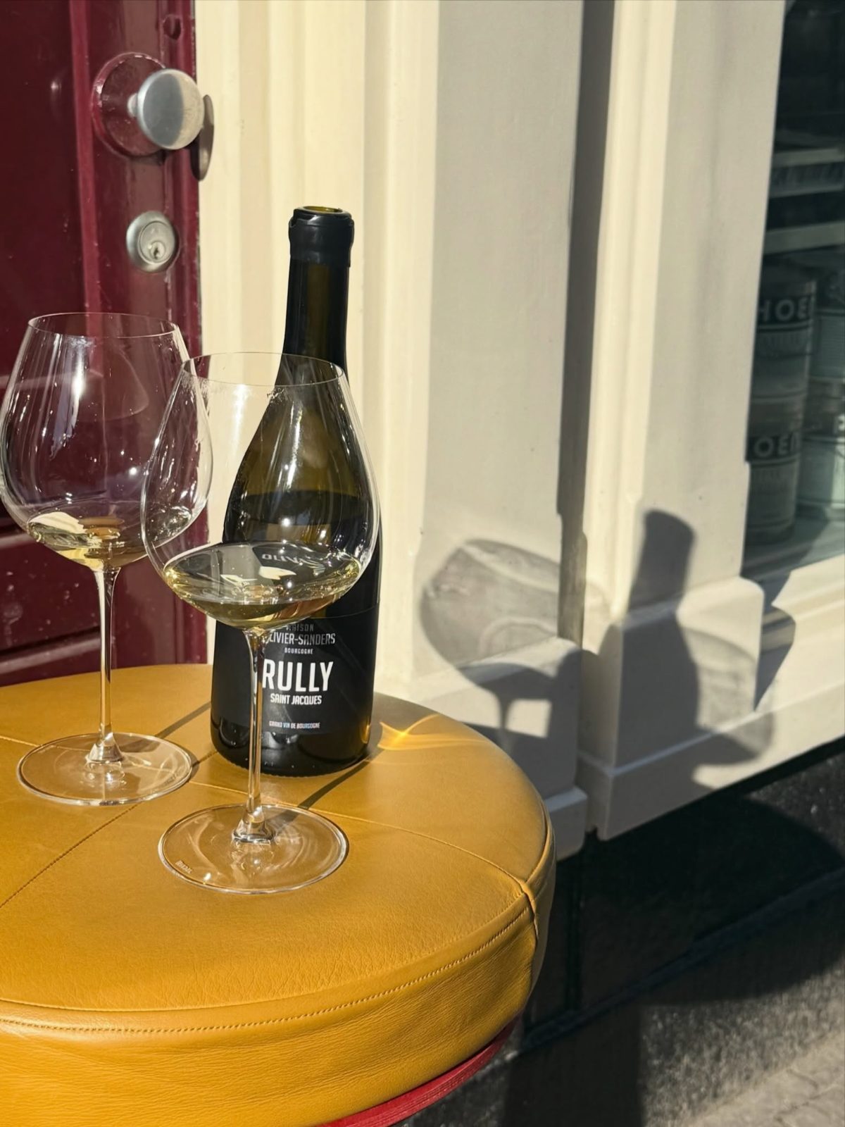 A bottle of white Burgundy with two wine glasses on a yellow table at Salut on Gerard Douplein